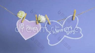 <strong>妇女节</strong>`快乐.. <strong>妇女节</strong>`纸上，挂在一根绳子上，靠近粉红色的纸心，蓝色的背景上有花。